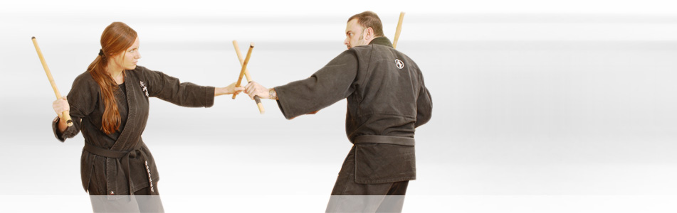 Two martial arts practitioners in dark gi training with wooden rattan sticks at Colorado Academy of Martial Arts